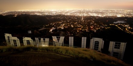 The back side of the HOLLYWOOD sign in Los Angeles stands in front of the city skyline at dusk.