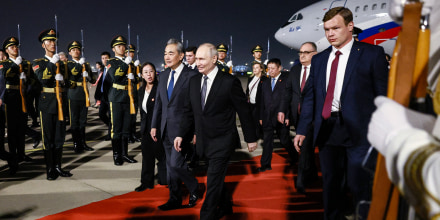 Vladimir Putin and Wang Yi walk along a red carpet extending from a plane parked in the background, with soldiers and other officials surrounding them