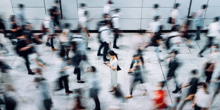 Image: Young woman using smartphone surrounded by commuters rushing by in subway station