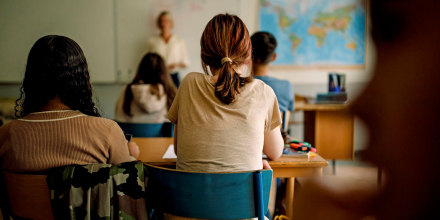 Rear view of teenage girls and boys learning in classroom