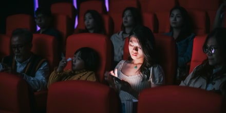 woman reading phone message during cinema movie show time in the dark ignoring and disturbing other audience around her