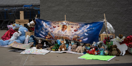 A memorial with balloons and stuffed animals in front of a Walmart.