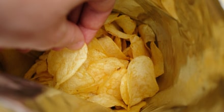 The girl takes crispy fried fatty potato chips from a package or pack. Chips in the hands of a woman, she eats them. The concept of an unhealthy diet and lifestyle, the accumulation of excess weight.