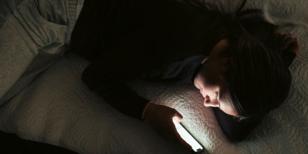Image: Directly above shot young woman text messaging on smart phone while lying on bed in bedroom at night