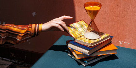 Hand reaching for a book on a stack with an hourglass on a table