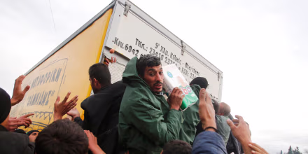 Image: Migrants try to get products from a truck at a makeshift camp on the Greek-Macedonian border near the village of Idomeni