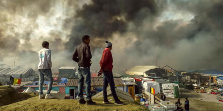 Image: Migrants stand on a hill overlooking the \"Jungle\" migrant camp in Calais