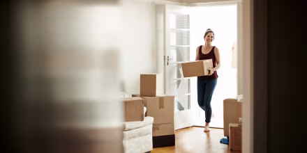 Image: Woman carrying boxes into her new home.