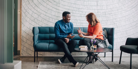Image: Businessman and woman taking while sitting on couch against wall at conference