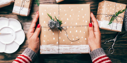 High Angle View Of Woman Holding Christmas Present On Table