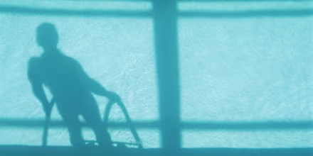 Man at poolside, low section, casting shadow on water, elevated view