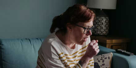 Woman Coughing While Sitting On Sofa At Home