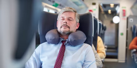 Tired businessman with neck pillow sleeping on passenger train