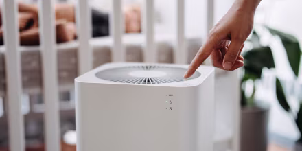 Close up hand of a mother turning on home air purifier for her newborn baby who is sleeping in the crib in the nursery. Fresh air. Cleaning and removing dust and bacteria. Healthier life and living concept