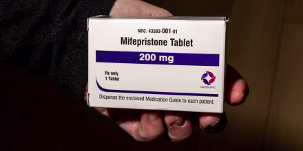 A hand holds a box of mifepristone