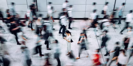Image: Young woman using smartphone surrounded by commuters rushing by in subway station