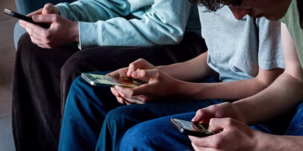 Three teenagers look at their smartphone screens on April 11, 2026.