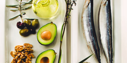 Still life of foods like olives, canola oil, mackerels, flaxseeds, avocado, and walnuts. 