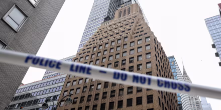 White tape with blue lettering reading POLICE LINE - DO NOT CROSS stretched in front of high-rise buildings in downtown Manhattan.