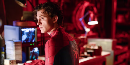 Tom Holland wearing a Spider Man suit and sitting at a work desk