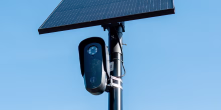 A Flock camera is mounted on a pole underneath a solar power panel