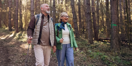 Older couple hiking in a sunlit landscape, equipped with trekking poles and backpacks, enjoying a calm and active lifestyle