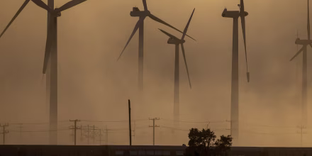 Wind turbines are partially obscured by a dust storm.