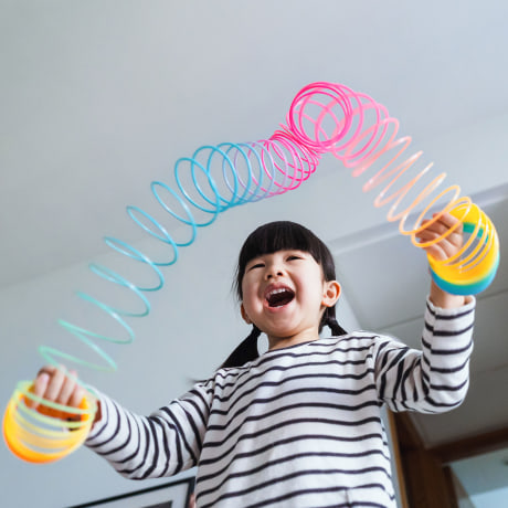 Low angle shot of a joyful little Asian girl playing with a colourful magic spring rainbow toy at home. Simple joy and happiness. Learning through play concept