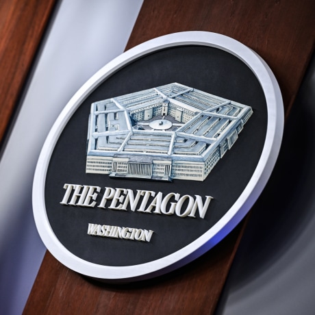 The Pentagon crest logo is on a wall next to an American flag