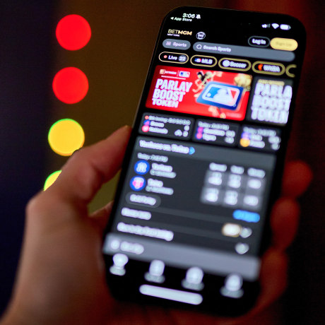 A hand holding a smartphone with a BET MGM gambling app showing on its screen