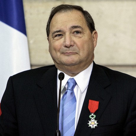 Abe Foxman standing at a microphone wearing a red ribboned medal on his lapel.