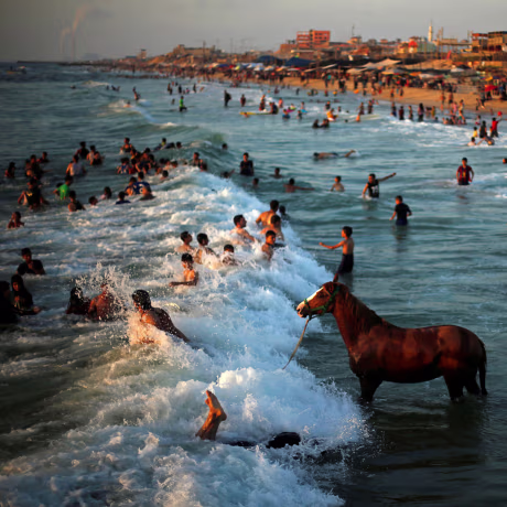 Image: Palestinian man washes his horse in the waters of the Mediterranean Sea as people swim on a hot day in the northern Gaza Strip