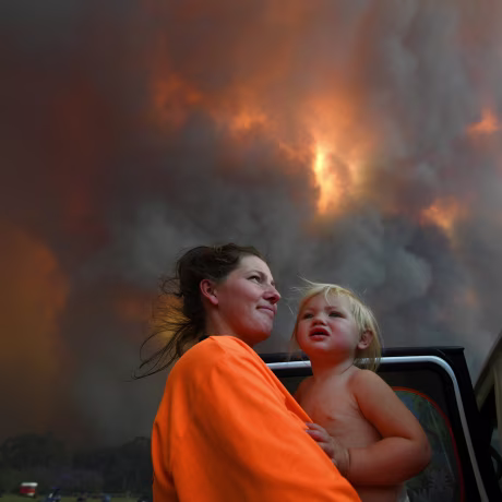 Image: Sharnie Moren and her 18-month-old daughter Charlotte look on as thick smoke rises from bushfires near Nana Glen
