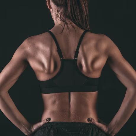 Rear view of female athlete wearing sports bra standing with hands on hip against black background
