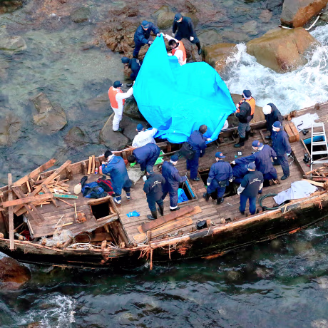 Police officers investigate a wooden boat marked with Hangul characters on Sado island, Niigata prefecture