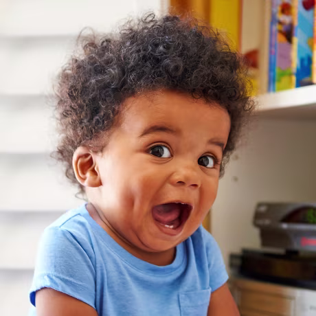 Surprised Black baby boy sitting on floor playing with books