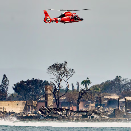 Image: A coastguard helicopter passing over damage caused by wildfires in Lahaina, Hawaii on Thursday, Aug. 10, 2023.