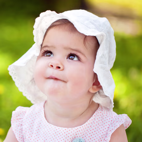 Cute baby girl with hat sitting on the grass.