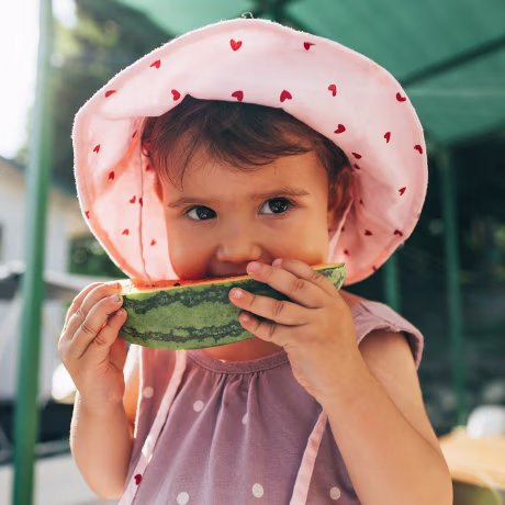 A Cute Baby Girl Eating Watermelon While Standing Outdoors