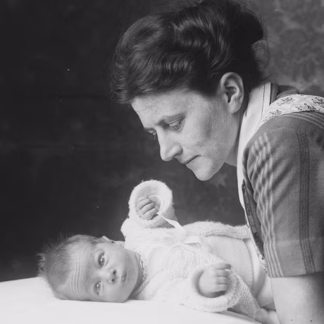 Black and white photo of caring mother leaning over her baby