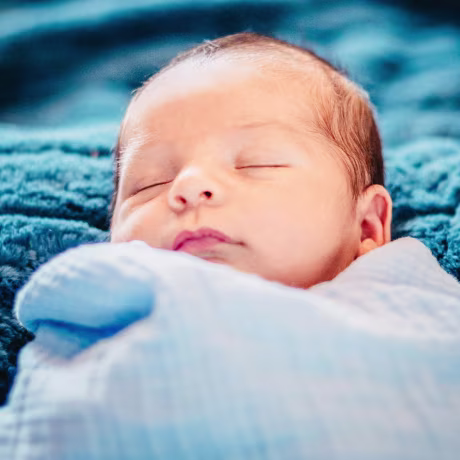 Latinx newborn baby in blue baby blanket.