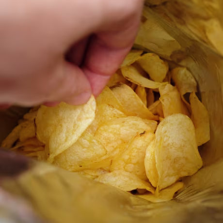 The girl takes crispy fried fatty potato chips from a package or pack. Chips in the hands of a woman, she eats them. The concept of an unhealthy diet and lifestyle, the accumulation of excess weight.
