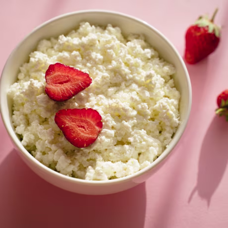Cottage cheese with strawberry fruits on pink table in bright sunlight
