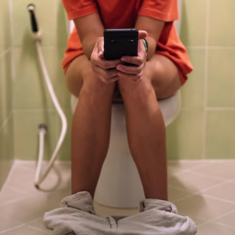 Woman sitting on a toilet holding a mobile phone in her hands