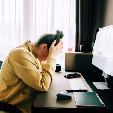 Woman working from home feeling stressed and frustrated, holding her head in her hands while sitting at her desk