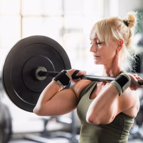 Focused mature female athlete lifting heavy barbell during cross training workout