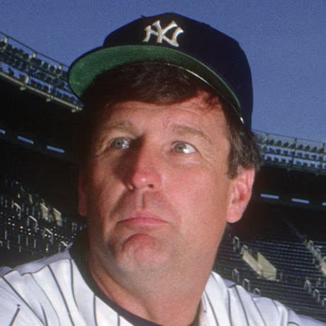 Tommy John sits on the baseball field in uniform, holding a catcher's mitt