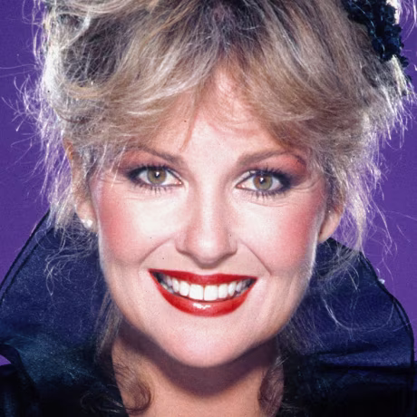 Shelley Fabares smiles for a portrait against a purple background