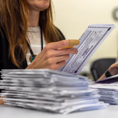 A woman extracts a mail-in ballot from an envelope.