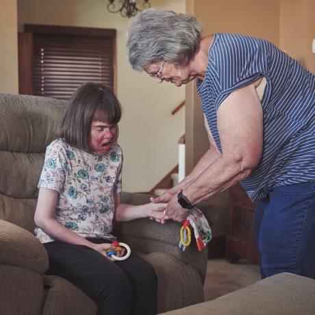 Image: Nancy Enstrom holding her daughter Anna's hand while assisting her at home.
